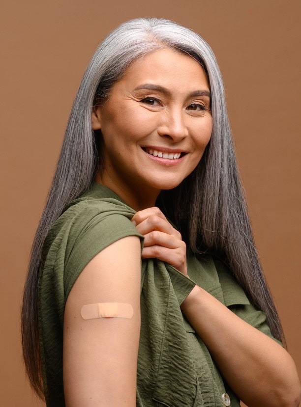 Smiling senior grey-haired woman with a medical patch after vaccination isolated on brown background, protecting hand with bandage after injection. Healthcare and medicine concept